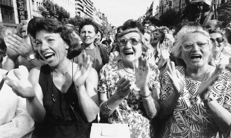 A black and white photo show three women in a crowd clap hands and cheer.