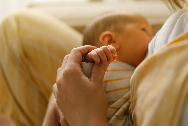 A mother holds the hand of her baby who is breastfeeding.