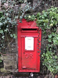 A bright red postbox set into an old stone wall. The letters GR appear on the front of the box and it is framed with ivy and other foliage.