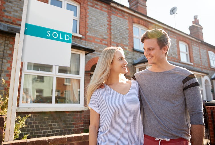 A couple standing in front of a house with a sold sign in front.